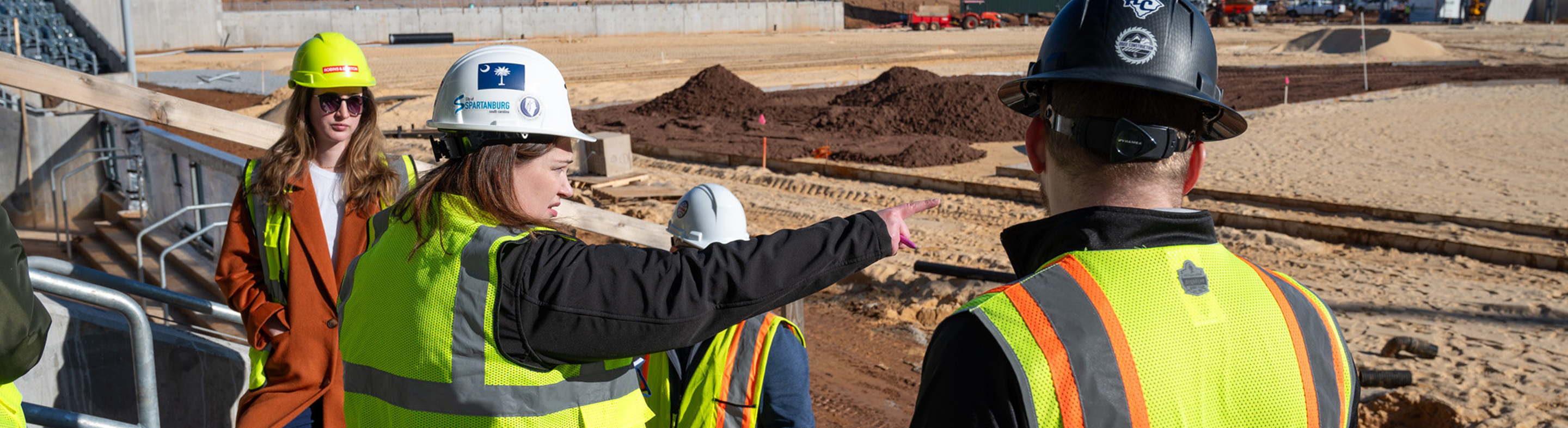 Image of people in construction vests and hardhats overlooking a construction site