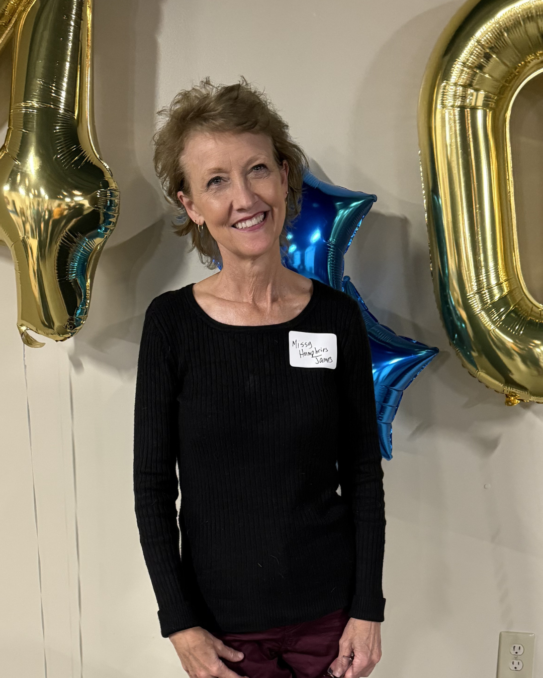 An older woman smiles and poses at a celebration.