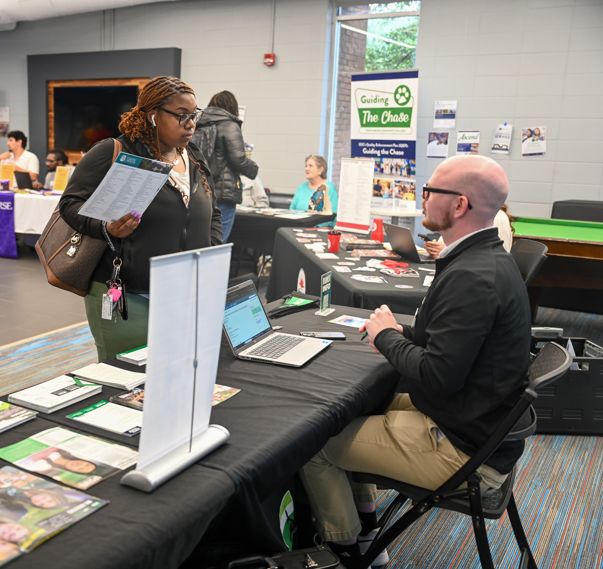 A young student speaks with a representative from a college, who is sitting behind a table.
